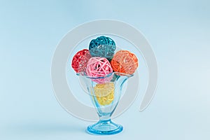 Rattan balls in form of ice cream scoops in glass cup on blue background minimalistic concept.