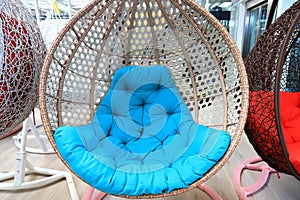 Rattan cocoon chair, garden furniture with blue cushion in store. Beautiful fashionable modern wicker furniture, sofa, rocking