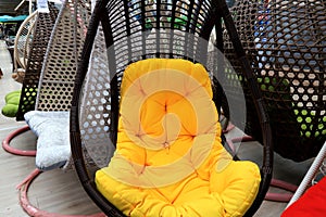 Rattan cocoon chair, garden furniture with yellow cushion in store. Beautiful fashionable modern wicker furniture, sofa, rocking