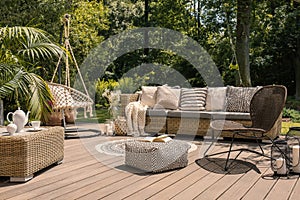 A rattan patio set including a sofa, a table and a chair on a wooden deck in the sunny garden.