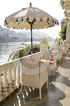 Rattan table and chairs under an umbrella in a street cafe on the shore near the lake in Udaipur, Rajasthan, India