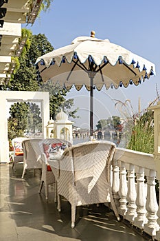 Rattan table and chairs under an umbrella in a street cafe on the shore near the lake in Udaipur, Rajasthan, India