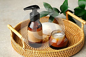 Rattan tray with natural cosmetics set. Amber glass shower gel dispenser bottle, moisturizer cream, organic soap and green leaf.