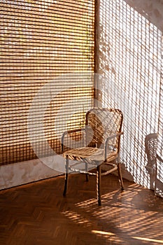 Rattan wicker chair with sunlight shining through wooden blinds