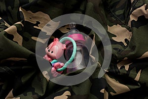 Rattle toy and baby bottle on military uniform. Love and war concept