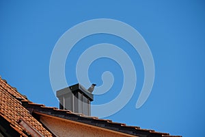 A raven sitting on a chimney on a red clay tile roof