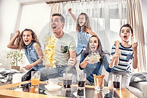 Raving fans cheering sports, as family of five watch football, or ice-hockey match on the TV at home, screaming from joy