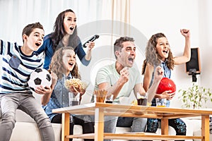 Raving fans cheering sports, as family of five watch football, match on the TV at home, screaming from joy