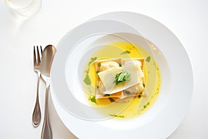 ravioli with butter sauce on a white plate, fork at the side