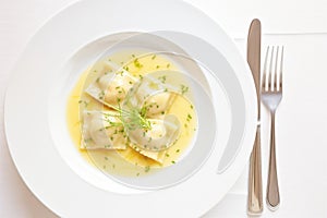 ravioli with butter sauce on a white plate, fork at the side