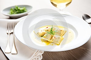 ravioli with butter sauce on a white plate, fork at the side