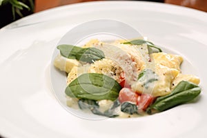 Ravioli pasta in cream sauce with basil and tomatoes, on a white plate, close-up.