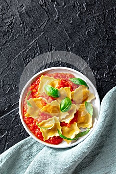 Ravioli with tomato sauce and fresh basil leaves on a plate, overhead