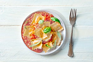 Ravioli with tomato sauce and fresh basil leaves on a plate, overhead