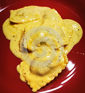 Raviolli. Cooked raviolli on a shiny red plate, 4 cheese sauce