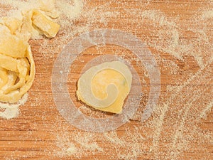 Raviolo in the shape of heart,covered with flour and placed on the wooden table.