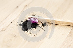 Raw activated charcoal powder on wooden background natural bamboo toothbrush inside it.