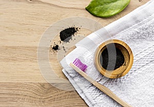 Raw activated charcoal powder in wooden cup and natural bamboo toothbrush .