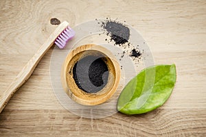 Raw activated charcoal powder in wooden cup and natural bamboo toothbrush next to it.