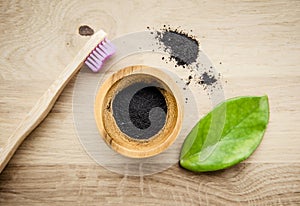 Raw activated charcoal powder in wooden cup and natural bamboo toothbrush next to it  green leaf for decoration.