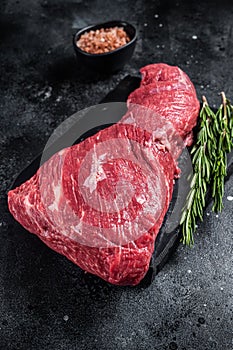 Raw American Tri Tip beef steak on marble board. Black background. Top view