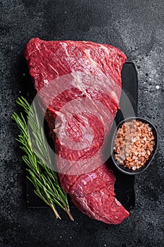 Raw American Tri Tip beef steak on marble board. Black background. Top view