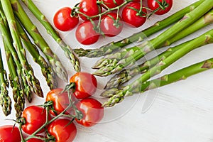 Raw asparagus stems and branches of cherry tomatoes on a off-white rustic table.