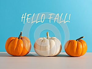 Raw Autumn pumpkins on wooden kitchen counter table against blue background with Hello Fall message