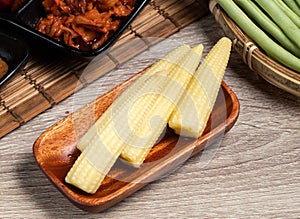 Raw Baby Corn served in dish isolated on wooden board side view of healthy food