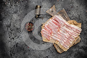 Raw bacon, bacon strips meat slice thin slicing pork fat meal on a dark background, ketogenic diet, place for text, top view