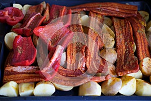 raw bacon slices with delicious curry sauce served on baking tray for oven grill, potatoes with meat, red paprika, green capsicum