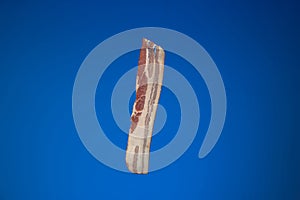 Raw bacon strip or slice . Close up studio shot, isolated on blue background
