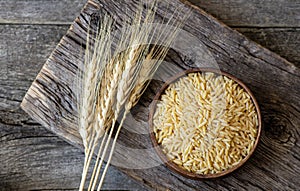 Raw barley noodle in bowl on wooden background with wheats