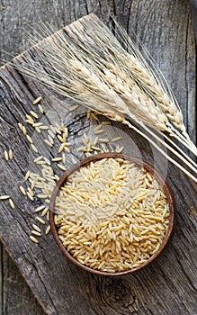 Raw barley noodle in bowl on wooden background with wheats