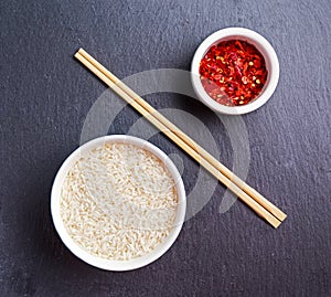 Raw basmati rice in a bowl with chillie flakes and Bamboo chopsticks on stone table