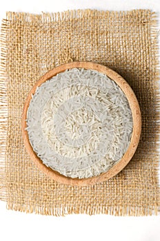 Raw basmati rice in a wooden bowl on burlap.