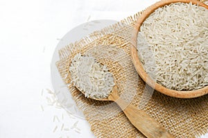 Raw basmati rice in wooden spoon and bowl on burlap.