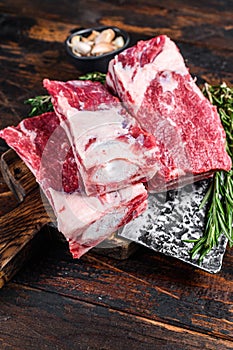 Raw beef calf short ribs meat on a butcher cutting board with cleaver. Dark wooden background. Top view