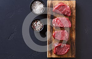 Raw beef filet mignon steaks with spices on wooden board at blac