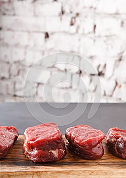 Raw beef filet mignon steaks on wooden board at black background against brick wall