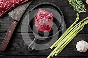 Raw beef fillet steaks with spices, on frying cast iron pan, on black wooden table background, top view flat lay