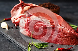 Raw beef heart meat on stone board with thyme and peppers