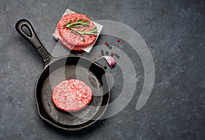 Raw Beef Meat Burger cutlets and spices in a cast-iron frying pan.