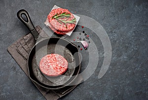 Raw Beef Meat Burger cutlets and spices in a cast-iron frying pan.