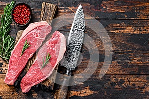 Raw beef meat cap sirloin steak on a cutting board. Dark wooden background. Top view. Copy space