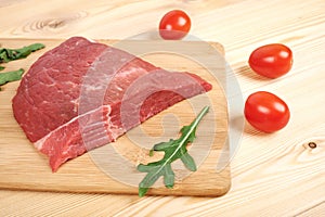 Raw beef meat on cutting board with vegetables on a wooden background