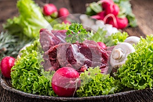 Raw beef meat with fresh vegetable. Sliced beef steak in lettuce salads radishes and mushrooms