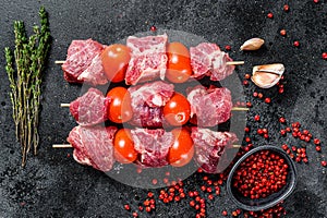 Raw beef meat kebab. BBQ with tomato and spices. Black background. Top view