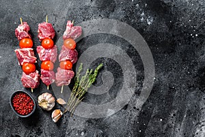 Raw beef meat kebab. BBQ with tomato and spices. Black background. Top view. Copy space
