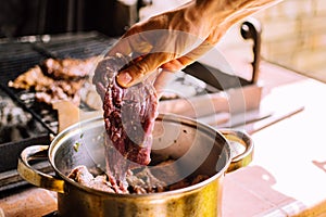 Raw beef meat pieces flavored with herbs in a pot. Man holding one of the pieces in his hand.